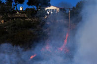 A wildfire burns near a home Wednesday, Oct. 13, 2021, in Goleta, Calif. A wildfire raging through Southern California coastal mountains threatened ranches and rural homes and kept a major highway shut down Wednesday as the fire-scarred state faced a new round of dry winds that raise risk of flames. The Alisal Fire covered more than 22 square miles (57 square kilometers) in the Santa Ynez Mountains west of Santa Barbara. (AP Photo/Ringo H.W. Chiu)