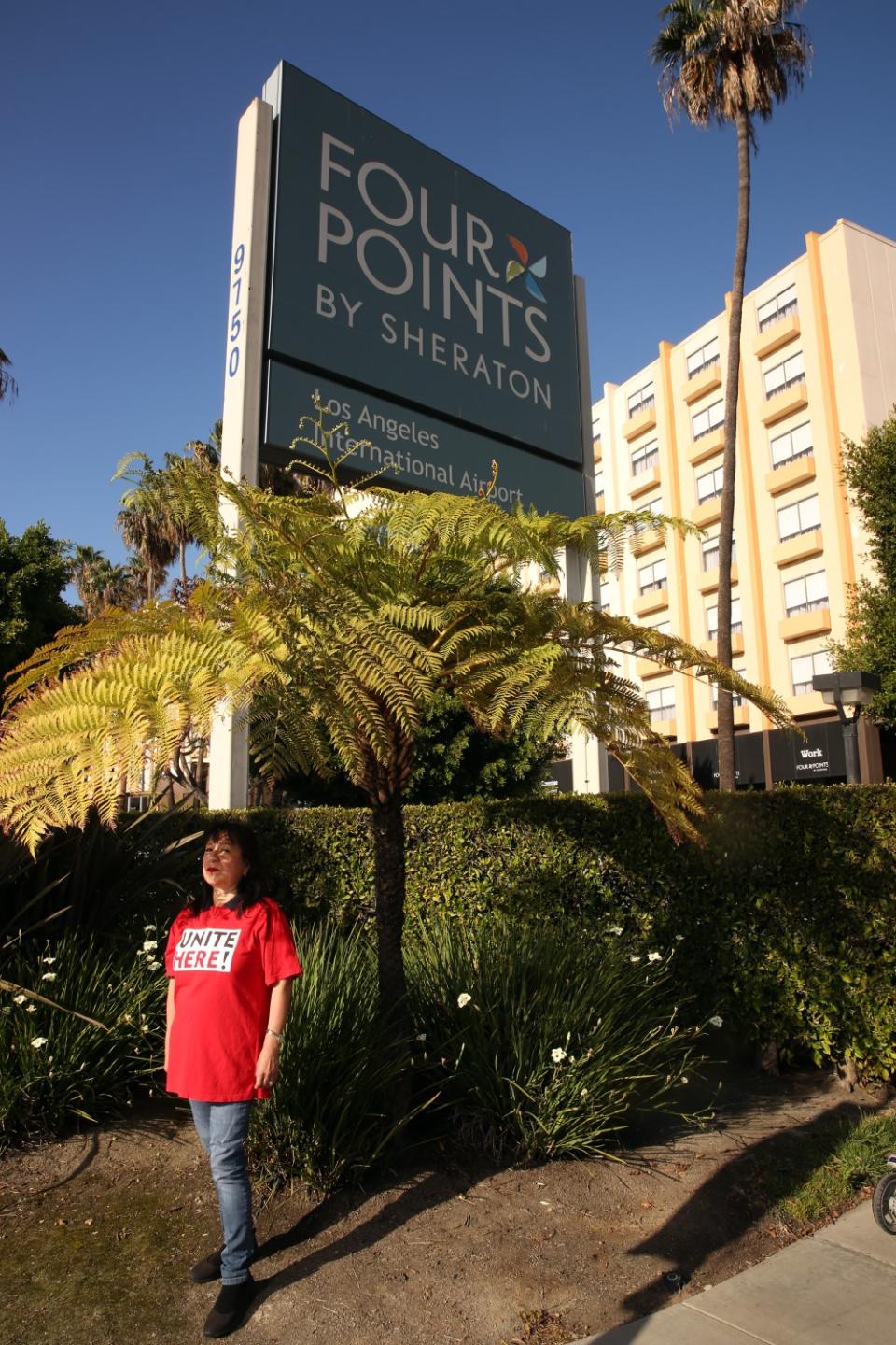 A woman stands near a sign that reads Four Points by Sheraton