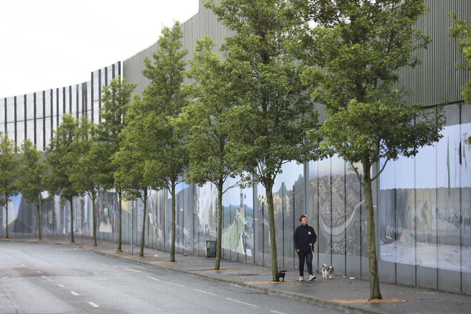 In this Tuesday, Oct. 15, 2019 photo a woman walks her dogs along the Protestant side of the peace wall that separates a Protestant area from a Catholic area in west Belfast, Northern Ireland. (AP Photo/Peter Morrison)