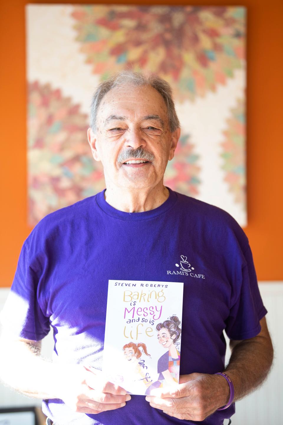 Steven Roberts, author of the book "Baking is Messy And So Is Life," poses for a portrait with a copy of his book at Rami's Cafe in Knoxville, Tenn. on Wednesday, Aug. 24, 2022.