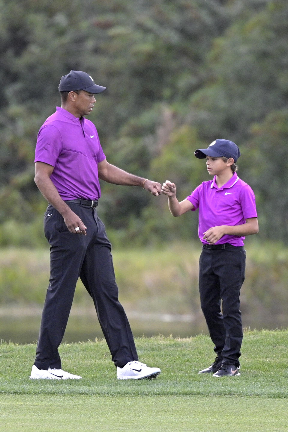 Tiger Woods, left, shares a fist-bump with his son Charlie after walking up their ball on the 14th fairway during the first round of the PNC Championship golf tournament, Saturday, Dec. 19, 2020, in Orlando, Fla. (AP Photo/Phelan M. Ebenhack)