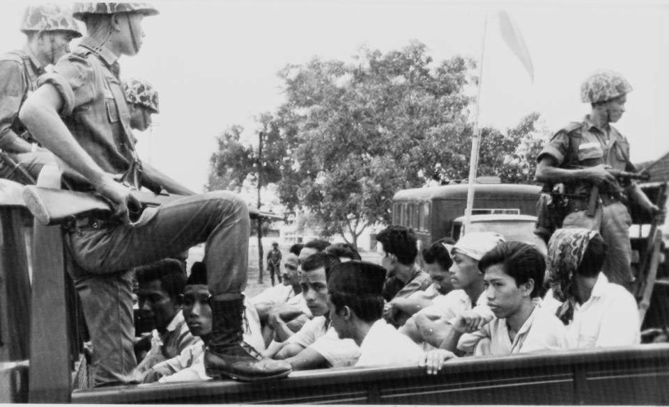 FILE - In this Oct. 30, 1965 file photo, members of the Youth Wing of the Indonesian Communist Party (Pemuda Rakjat) are guarded by soldiers as they are taken by an open truck to prison in Jakarta after they were rounded up by the army following a crackdown on communists after an abortive coup d'etat against President Sukarno's government earlier in the month. A new American-directed documentary, "The Act of Killing," challenges widely held views about hundreds of thousands of deaths carried out across Indonesia from 1965 to 1966 in the name of fighting communism. It explores the country's darkest open secret by allowing former mass killers to re-enact their horrors on screen. (AP Photo/File)