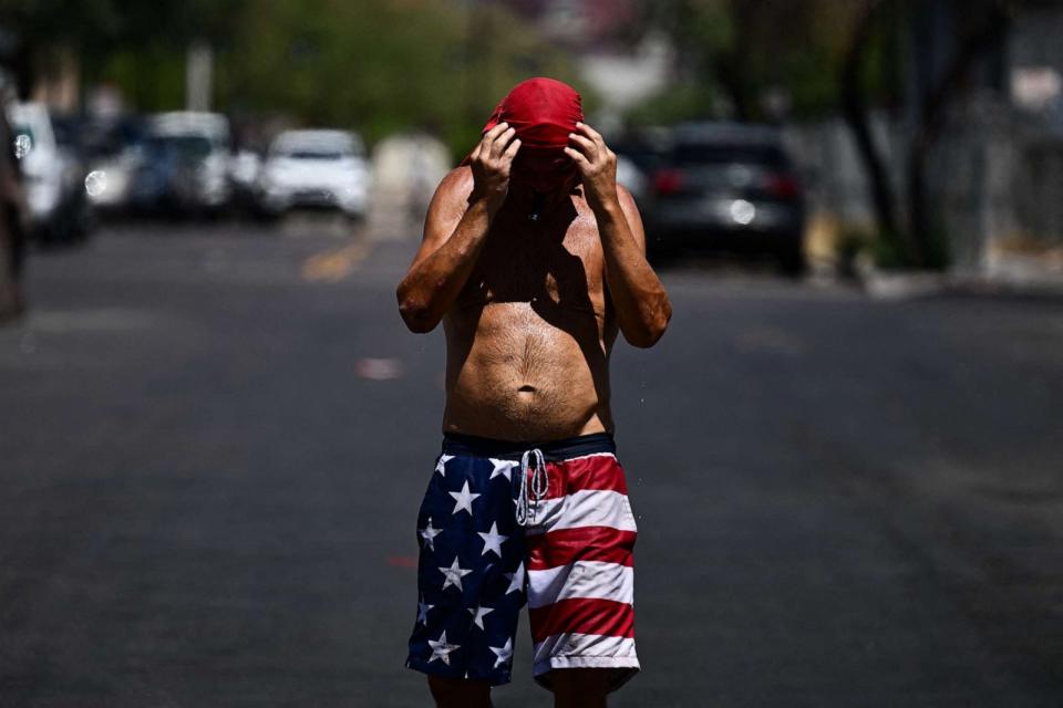 PHOTO: Water drips from a person as they grasp at their head covering while walking in the sun through 'The Zone,' a vast homeless encampment where hundreds of people reside, during a record heat wave in Phoenix, Arizona on July 18, 2023. (Patrick T. Fallon/AFP via Getty Images)