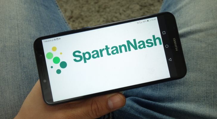 A photo of a hand holding a phone with the Spartan Nash logo on it.