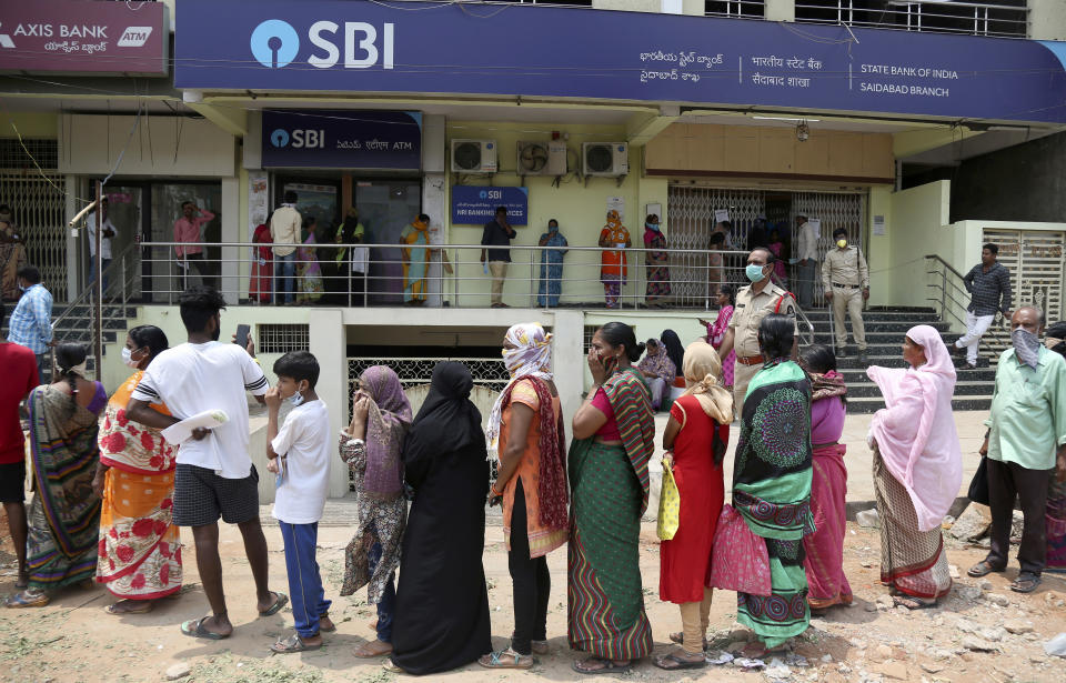 FILE- In this April 6, 2020 file photo, Indians queue up outside a bank to withdraw relief money deposited into their accounts by the government during lockdown to prevent the spread of new coronavirus in Hyderabad, India. India, a bustling country of 1.3 billion people, has slowed to an uncharacteristic crawl, transforming ordinary scenes of daily life into a surreal landscape. The country is now under what has been described as the world’s biggest lockdown, aimed at keeping the coronavirus from spreading and overwhelming the country’s enfeebled health care system. (AP Photo/Mahesh Kumar A, File)