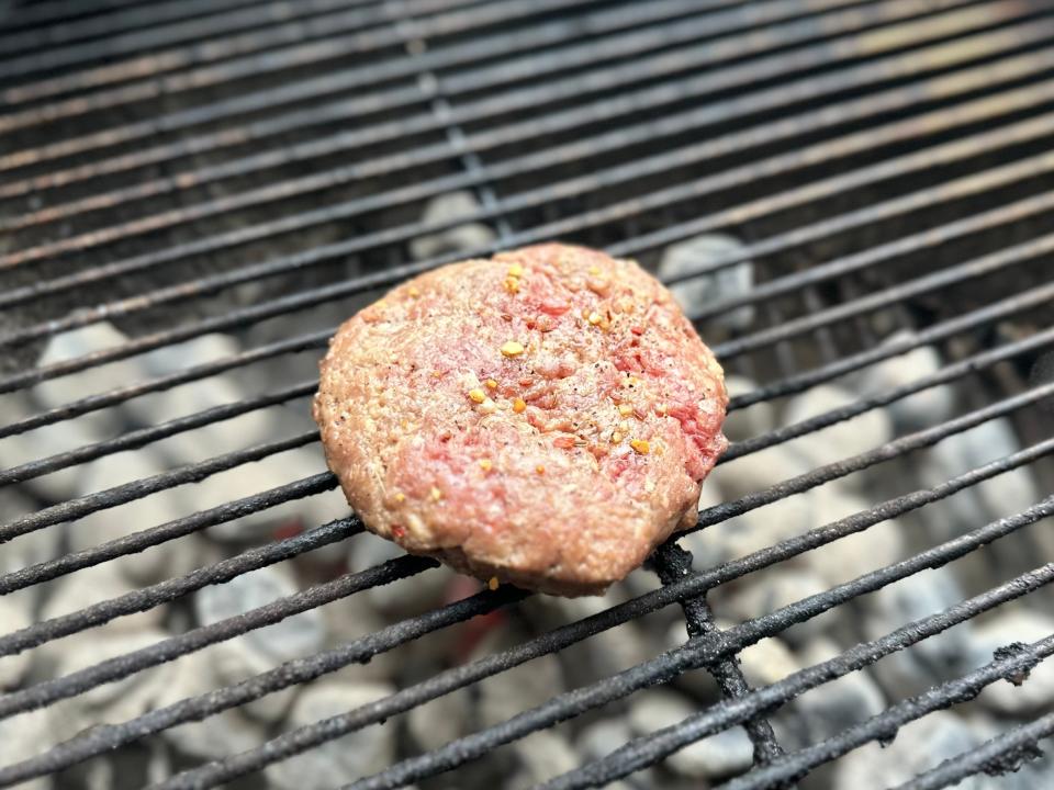 raw burger patty cooking on a charcoal grill