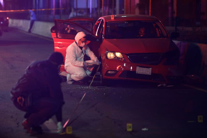 A forensic technician and a police officer work at a crime scene stand where unknown assailants attacked a vehicle, in Ecatepec de Morelos