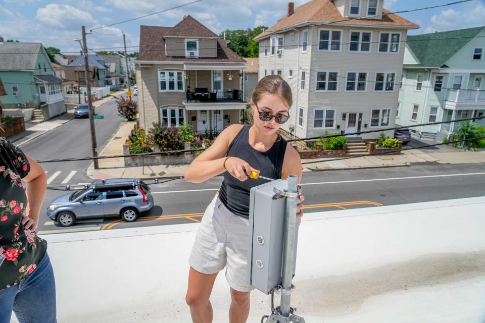 Grace Berg, coordinator of the Breathe Providence study, removes the cover from an air quality monitor on the roof of the Child & Family Rhode Island building on Eddy Street.