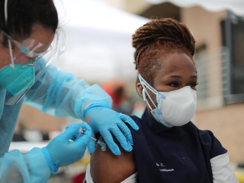 A health worker in blue protective gear and gloves injects a vaccine in a woman's arm.