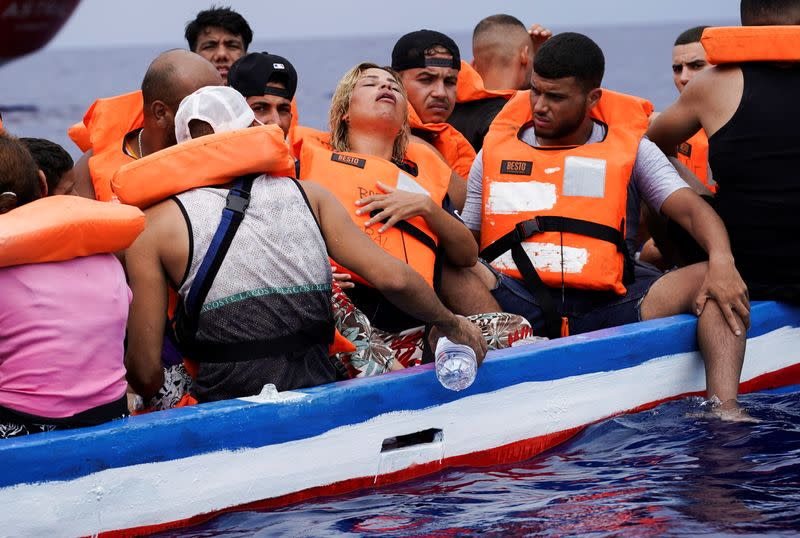 Migrantes esperan en una embarcación de madera a ser rescadatos por la Guardia Costiera italiana en el Mediterráneo