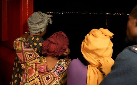 Rescued migrants look at lights on the island of Lampedusa from aboard the Ocean Viking - Credit: AP Photo/Renata Brito