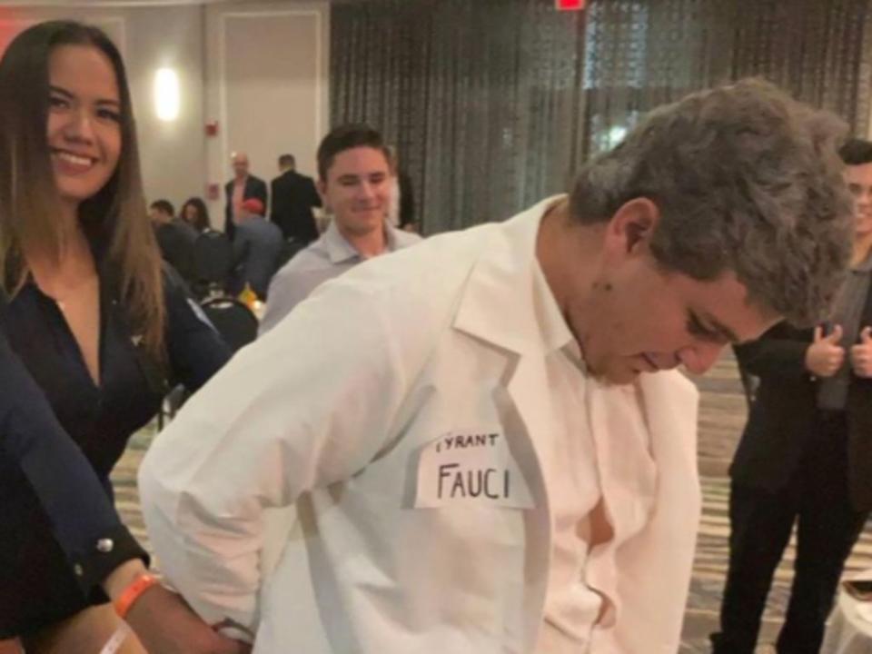 A woman dressed as a cop pretends to arrest a man dressed as Dr Anthony Fauci (Twitter @patriottakes)