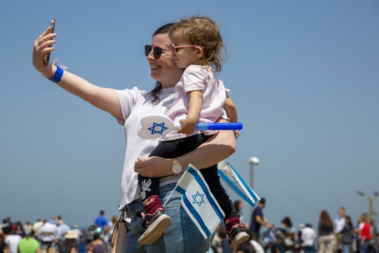 Una mujer sonríe mientras carga a un niño en Israel durante el Día de la Independencia el 15 de abril 2021. El país suspendió el uso de tapabocas obligatorio. 