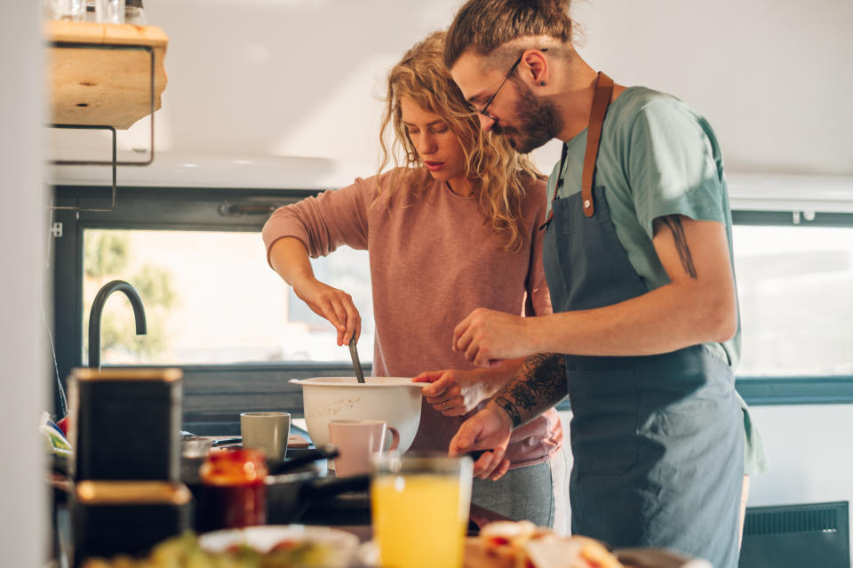 Cute romantic couple cooking together and making breakfast while laughing and spending time together in the kitchen. Young cheerful spouses enjoying morning time together. Making pancakes. Copy space