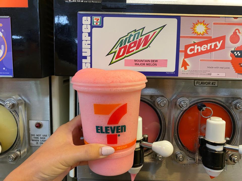 A hand filling up a large 7/11 cup with mountain dew major lemon slurpee