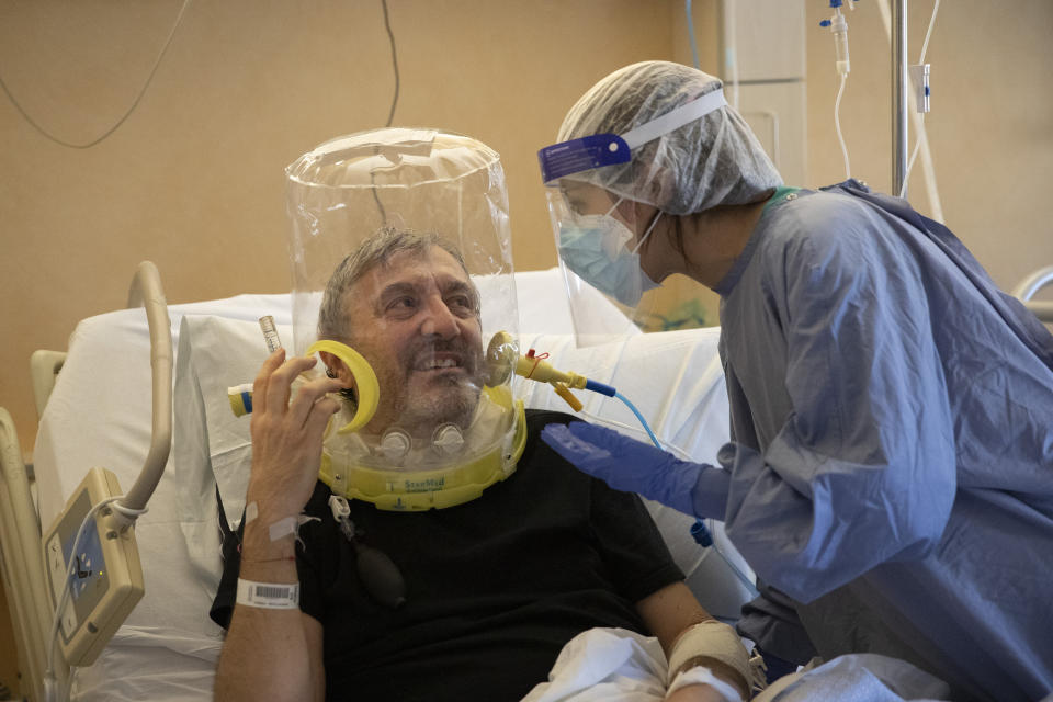 60-year-old Nazzareno Santilli, breathing under oxygen CPAP (continuous positive air pressure) headgear ventilation, smiles back to Dr. Elisabetta Teti in the sub-intensive COVID-19 unit of the Tor Vergata Polyclinic Hospital, in Rome, Saturday, Nov. 7, 2020. Communication is challenging when patients wear oxygen helmets and Teti is covered by layers of protective gear. (AP Photo/Alessandra Tarantino)