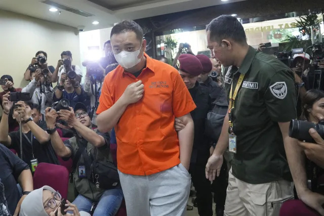 Chinese fugitive identified only by his initial LQ wears a mask escorted by Immigration officers before a news conference in Jakarta, Indonesia, Thursday, Oct. 10, 2024. (AP Photo/Tatan Syuflana)