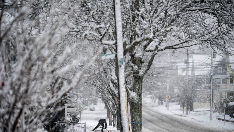 A worker shovels snow off a sidewalk Tuesday, Feb. 13, 2024, in Providence, R.I. Winter weather warnings and colder temperatures are expected to hit over half the U.S. before the official start of spring.