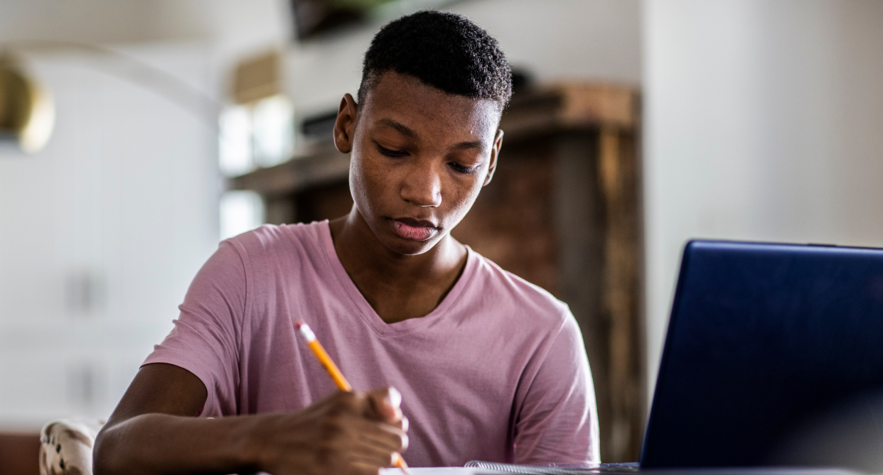 teenager boy wearing lavender shirt sitting with pencil in front of laptop computer, laptops for school