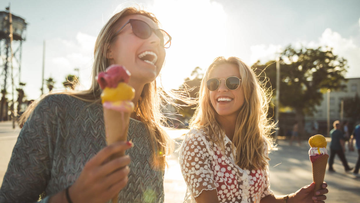 Two women enjoying summer holiday walk and eating an ice cream.