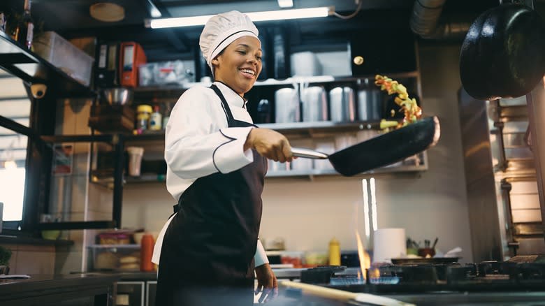 A smiling cook preparing a meal in a professional kitchen