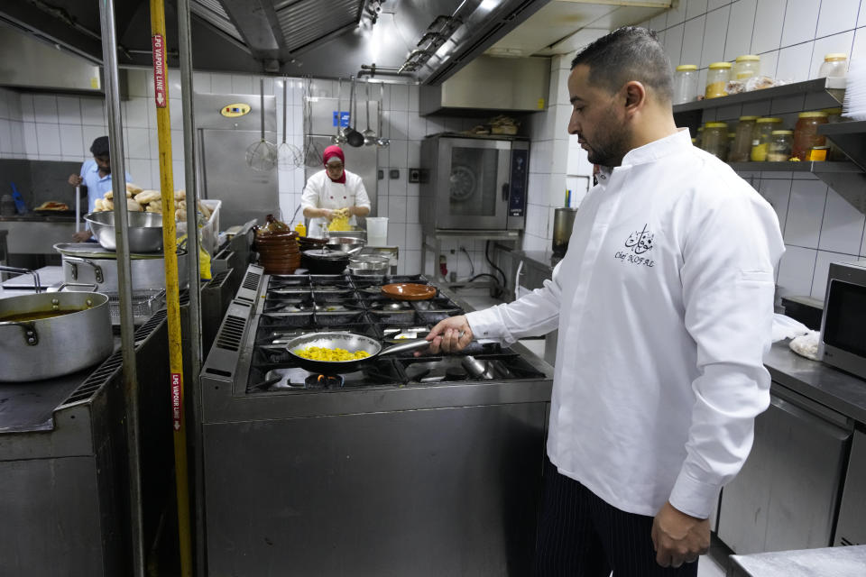 Moroccan chefs Naoufel Farih, right, and Fatma Taouzani, center, prepare food in the kitchen inside the Marrakech restaurant, in Doha, Qatar on Sunday Dec. 4, 2022. (AP Photo/Ashley Landis)