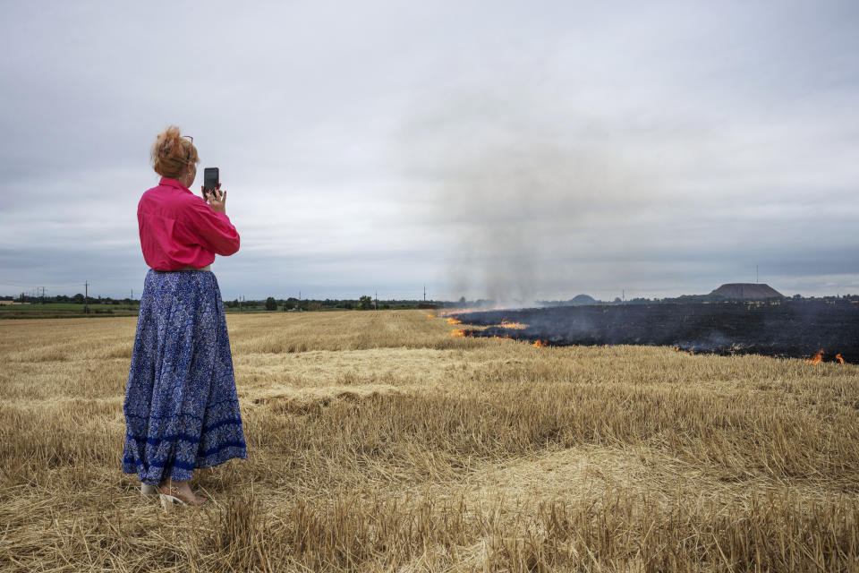 Medic volunteer Nataliia Voronkova, takes a photo of grain fields burning, on the outskirts of Kurakhove, Donetsk region, eastern Ukraine, Thursday, July 21, 2022. Voronkova has dedicated her life to aid distribution and tactical medical training for soldiers and paramedics, working on front line of the Donetsk region since the war began in 2014. (AP Photo/Nariman El-Mofty)