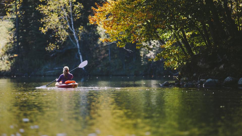 woman kayaking on lake during peak foliage