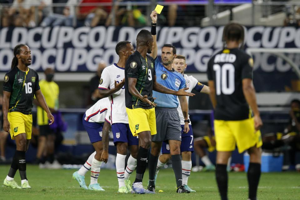 Jamaica forward Cory Burke (9) is issued a yellow card by referee Cesar Ramos, right center, as Daniel Johnson (16) and Bobby Reid (10) look on in the first half of a CONCACAF Gold Cup quarterfinals soccer match, Sunday, July 25, 2021, in Arlington, Texas. Burke received the card for knocking down United States midfielder Gianluca Busio during play. (AP Photo/Brandon Wade)