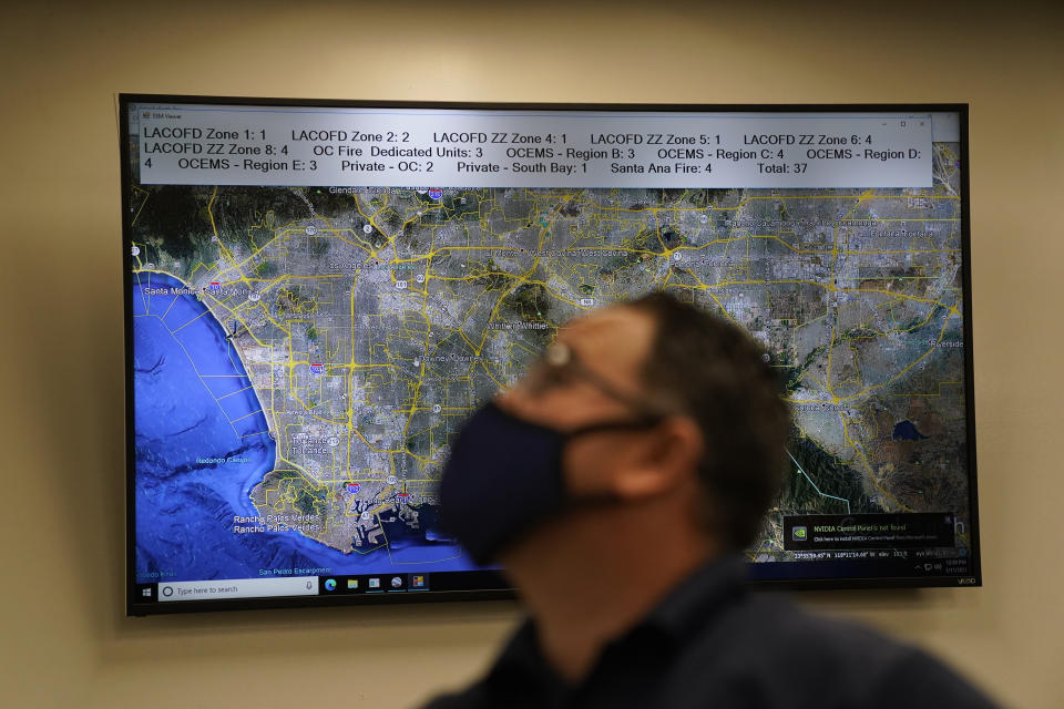 Dispatch Supervisor Erick Aguilar stands in front of a screen showing the map of Los Angeles County while working in Care Ambulance Service's communication center in Santa Fe Springs, Calif., Saturday, Jan. 9, 2021. Dispatchers play chess with ambulances all day. When one gets stuck at a hospital for eight, 10 or 12 hours, the dispatchers must reposition the others to cover its area. When an EMT reports a positive COVID-19 test, the dispatchers must find a way to cover the ambulance's calls if the whole crew must quarantine. (AP Photo/Jae C. Hong)