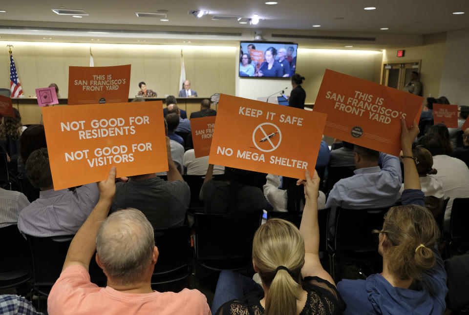 FILE - In this April 23, 2019 file photo people opposed to a proposed homeless shelter hold up signs during a meeting of the Port Commission in San Francisco. San Franciscans should put aside their political differences and support finding homes for more than 1,000 homeless people, according to a public engagement campaign beginning Thursday, July 25, 2019. (AP Photo/Eric Risberg, File)