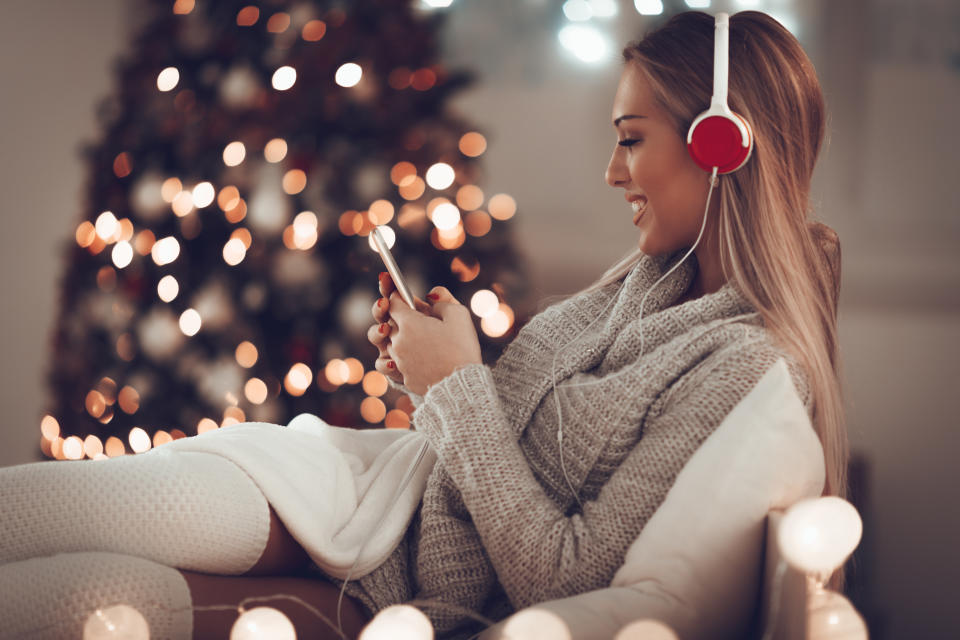 Frau sitzt auf Couch - Weihnachtsbaum im Hintergrund - mit roten Kopfhörer und lächelt ihr Smartphone an