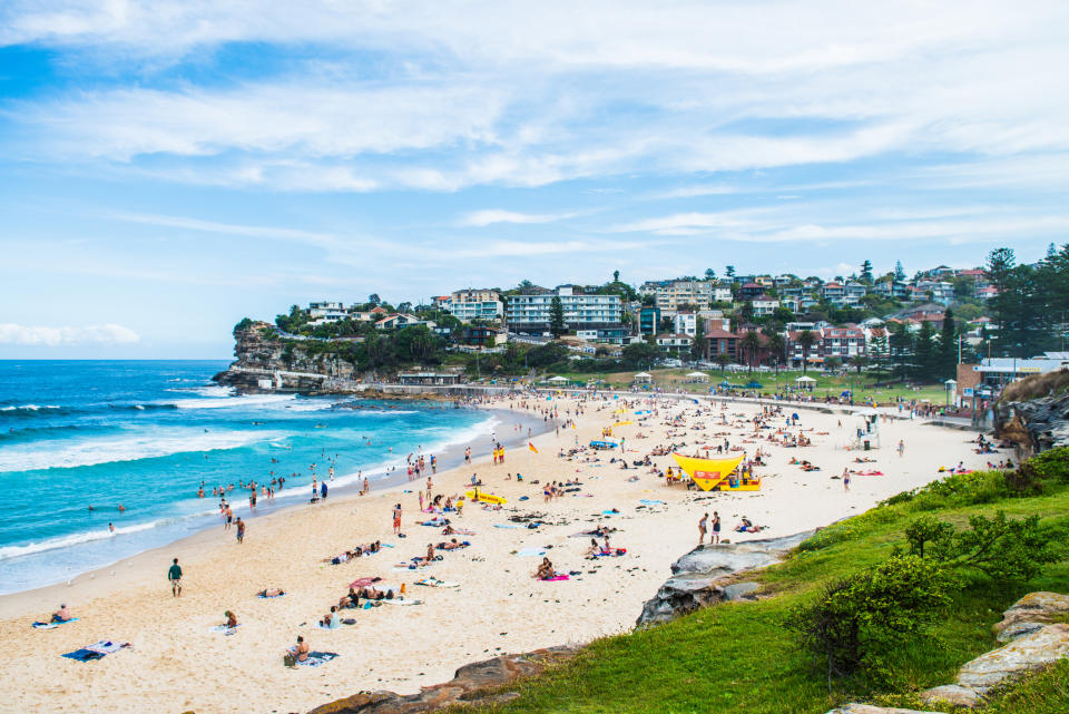 A beach scene with people, greenery-covered cliffs, and a clear sky