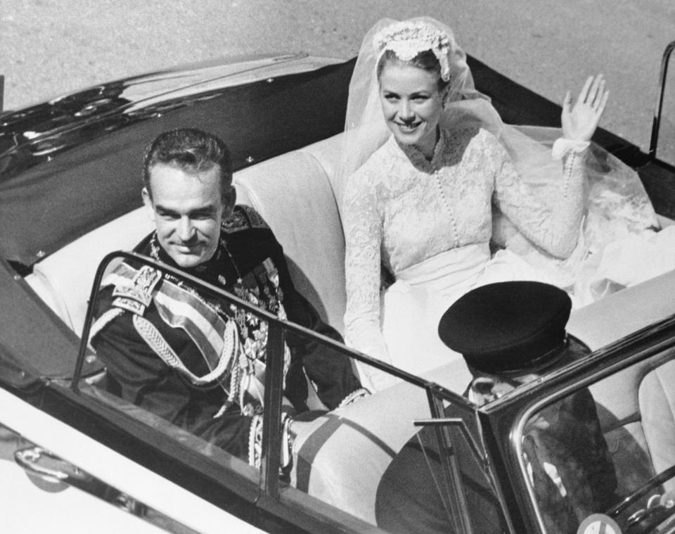 Grace Kelly waves to admirers as she and Prince Rainier are picture in an open car.