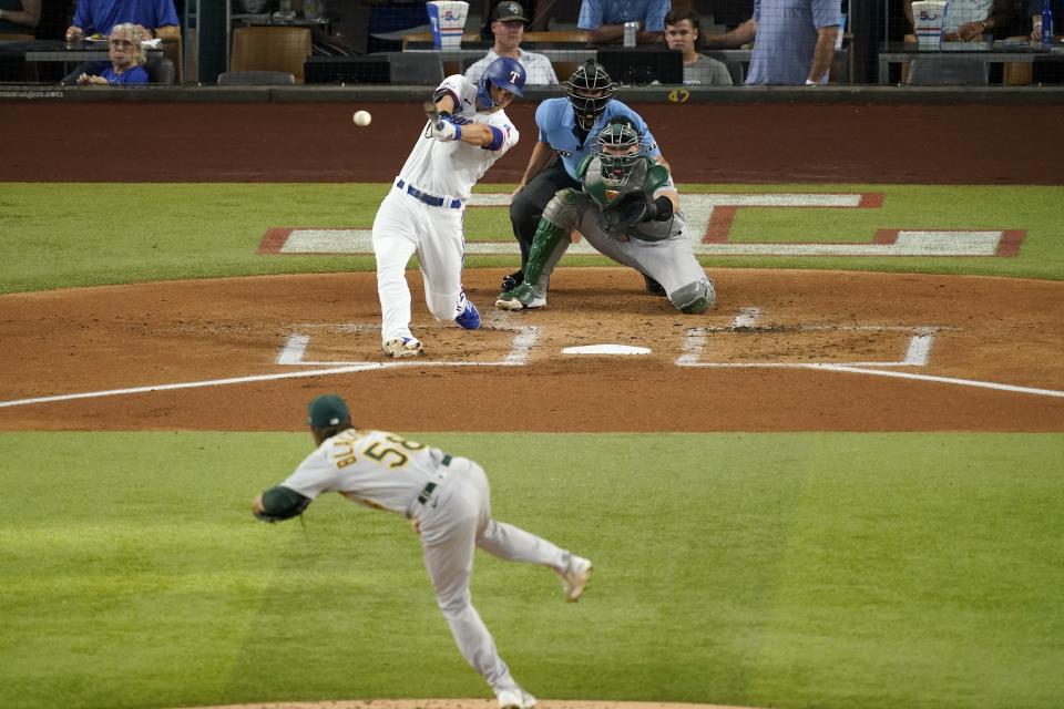 Texas Rangers' Corey Seager connects for a run-scoring single off a pitch from Oakland Athletics starting pitcher Paul Blackburn (58) as catcher Sean Murphy and umpire Johbn Tumpane look on in the first inning of a baseball game, Wednesday, July 13, 2022, in Arlington, Texas. (AP Photo/Tony Gutierrez)