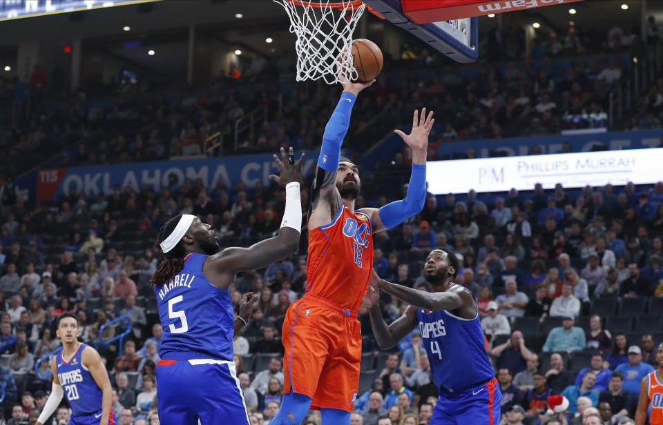 Oklahoma City Thunder center Steven Adams (12) goes up for a basket between Los Angeles Clippers forward Montrezl Harrell (5) and forward JaMychal Green (4) during the second quarter of an NBA basketball game Sunday, Dec. 22, 2019, in Oklahoma City. (AP Photo/Alonzo Adams)