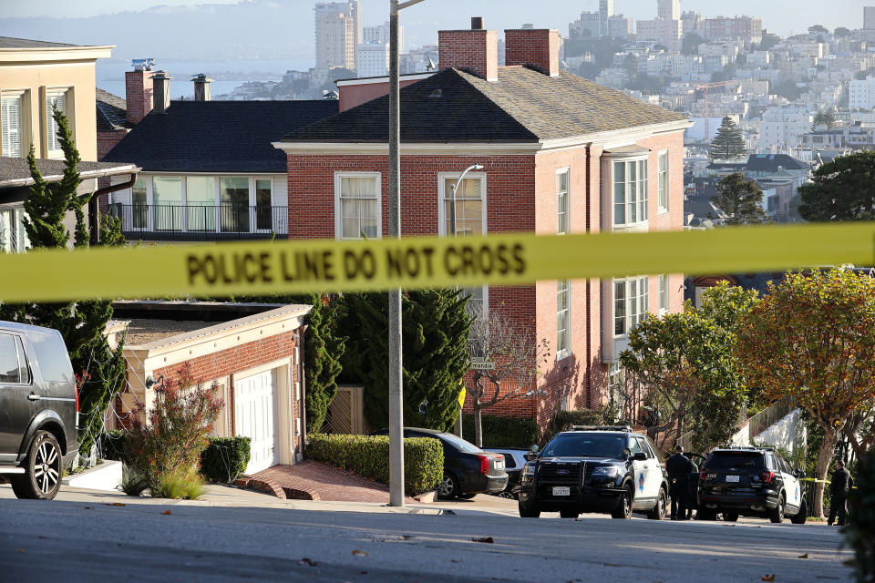 Police tape on the street outside the Pelosi home following the attack, with the San Francisco skyline in the background.
