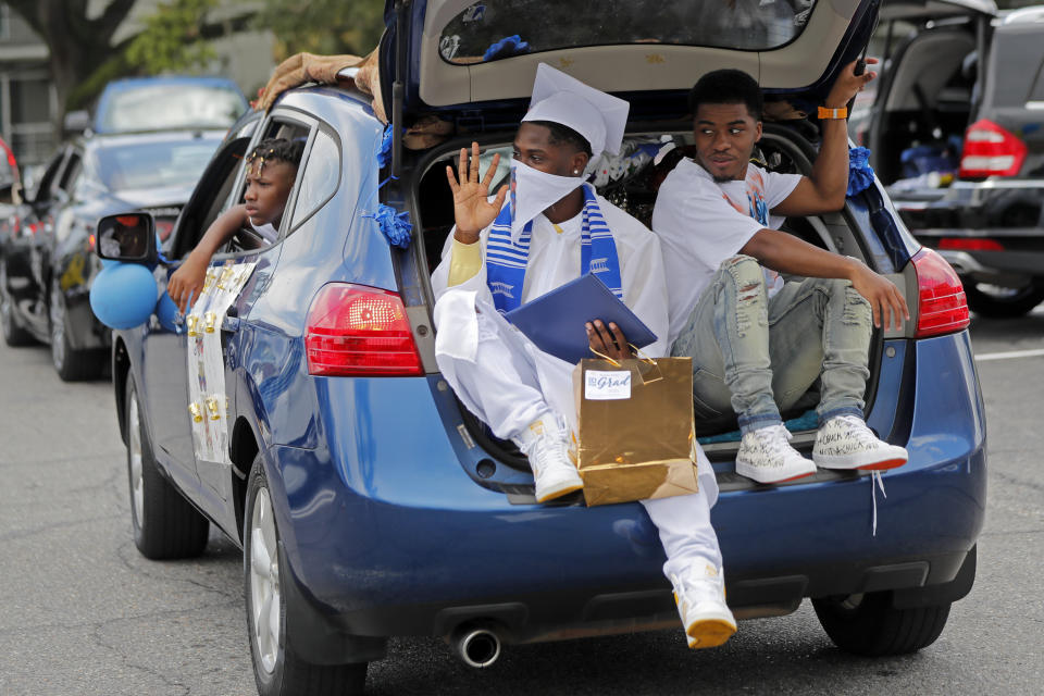 Graduate Deaundre Rumley waves as he rides in the back of a car with his brother Patrick Polk, after receiving his diploma as the New Orleans Charter Science and Math High School class of 2020 holds a drive-in graduation ceremony as a result of the COVID-19 pandemic, outside Delgado Community College in New Orleans, Wednesday, May 27, 2020. Students and family got out of their cars to receive diplomas one by one, and then held a parade of cars through city streets. (AP Photo/Gerald Herbert)