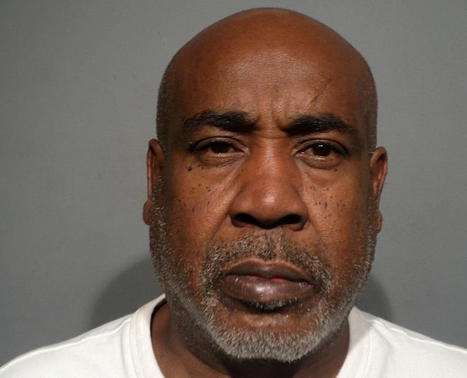 A mug shot of an older Black man with a bald head, trim gray beard, and white T-shirt.