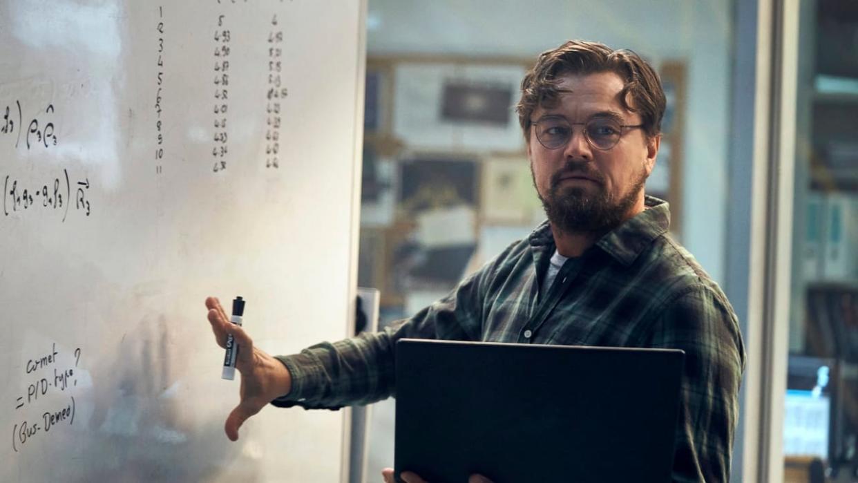 Leonardo DiCaprio holding a computer next to a white board