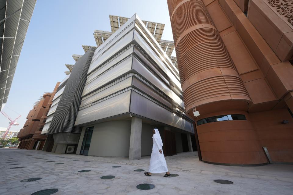 A man walks past a building with solar panels at Masdar City near Abu Dhabi, United Arab Emirates, as Dubai hosts the COP28 U.N. Climate Summit, Friday, Dec. 8, 2023. (AP Photo/Kamran Jebreili)