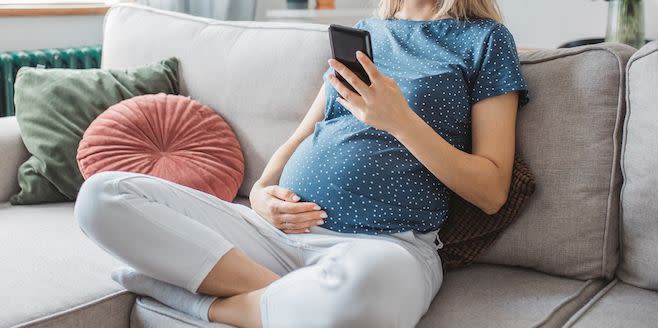 young pregnant woman at home sat on the sofa with a hand on her bump