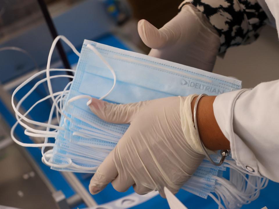 Bunch of disposable face masks held by person wearing gloves and white lab coat