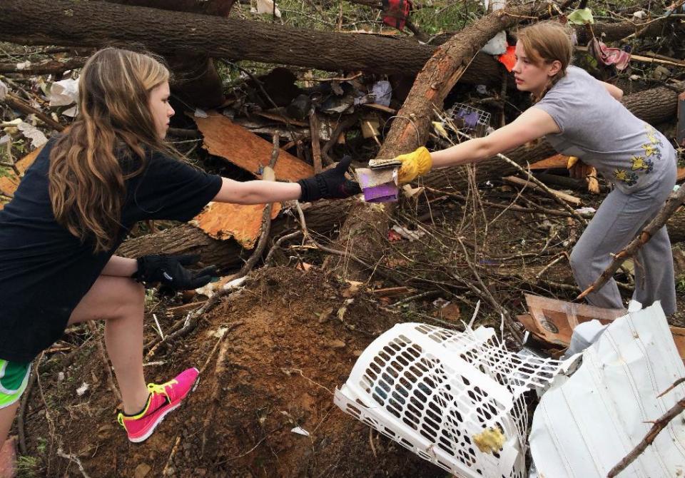 In this Monday, April 28, 2014 photo, Emily Tittle, right, hands Leah, last name not given, an item as they pick through rubble after a tornado stuck Sunday, in Paron, Ark. Tittle said she, her eight siblings and her parents went for safety under the stairs in the two-story house, but only half of them made it before the walls were obliterated by the twister that left just the foundation behind. Her father, Rob Tittle, and two sisters, Tori, 20, and Rebekah, 14, were killed in the storm. (AP Photo/Christina Huynh)