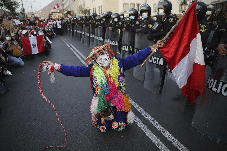 FILE - A folk artist performs alongside a cordon of police outside the Congress building, as Peruvians wait for news on who will be the country's next president, in Lima, Peru, Nov. 15, 2020. Peru at the time had three different presidents in a single week after one was impeached by Congress and protests forced his successor to resign. (AP Photo/Rodrigo Abd, File)