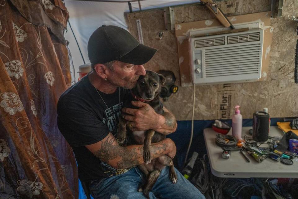 Nikki Buckles, a former carpenter, sits with his beloved dog Opium near a small air conditioner he hooked up to a generator to stay cool in a small room inside a tent and wooden makeshift shelter on Tuesday. He was worried about leaving his possessions to go to a cooling center but admitted, if he felt the dog is in danger of the heat, he might go.