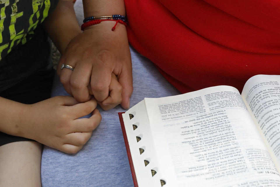 Eugenia Rodriguez holds the hand of her youngest son, Aaron, 6, while reading from the Bible in her house, Friday, July 2, 2021, in Chicago's Little Village neighborhood. Rodriguez hasn't been eligible for insurance coverage after overstaying a visitor visa from Mexico. She used to wake up every two or three hours at night to check on her mother. Since getting health insurance through the Illinois program, her mother has all the medications she needs. (AP Photo/Shafkat Anowar)