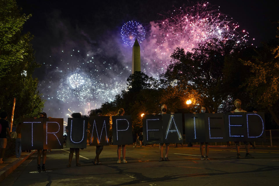 Protesters hold a lighted sign as fireworks light up the sky around the Washington Monument after President Donald Trump delivered his acceptance speech at the White House to the 2020 Republican National Convention, Thursday, Aug. 27, 2020. (AP Photo/Carolyn Kaster)