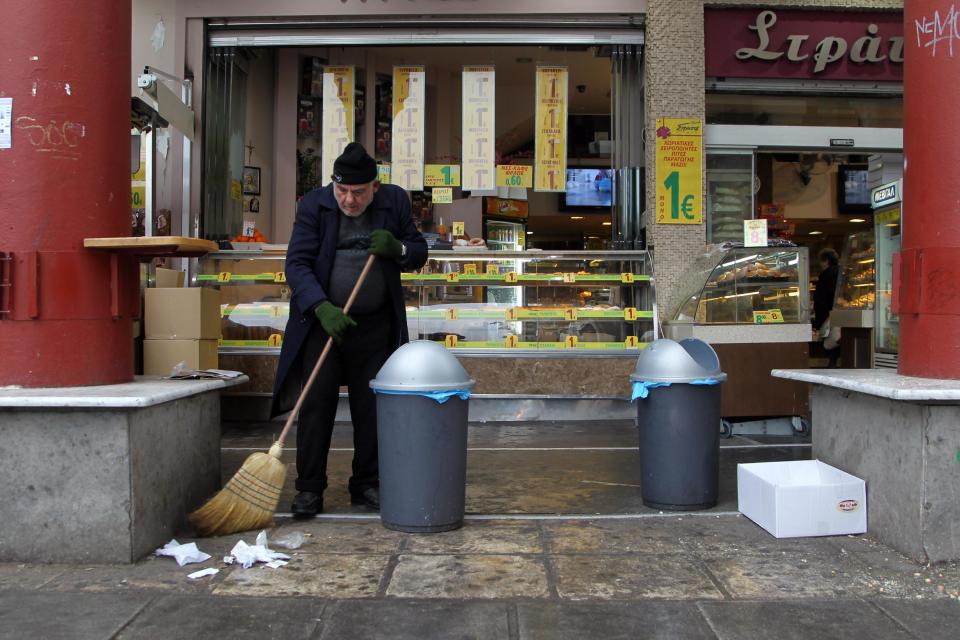 A man sweeps the pavement in the northern Greek port city of Thessaloniki, Wednesday, Jan. 15, 2014. Greece expects to post a budget surplus for 2013 once interest payments on existing debt are stripped out, according to the Ministry of Finance, however, if interest payments are included, then the country is still having to borrow money to make ends meet. (AP Photo/Nikolas Giakoumidis)