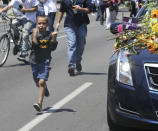 A young boy man runs beside the hearse carrying the body of Muhammad Ali with flowers as it drives down Broadway toward Cave Hill Cemetery in Louisville. REUTERS/Michael Clevenger/POOL